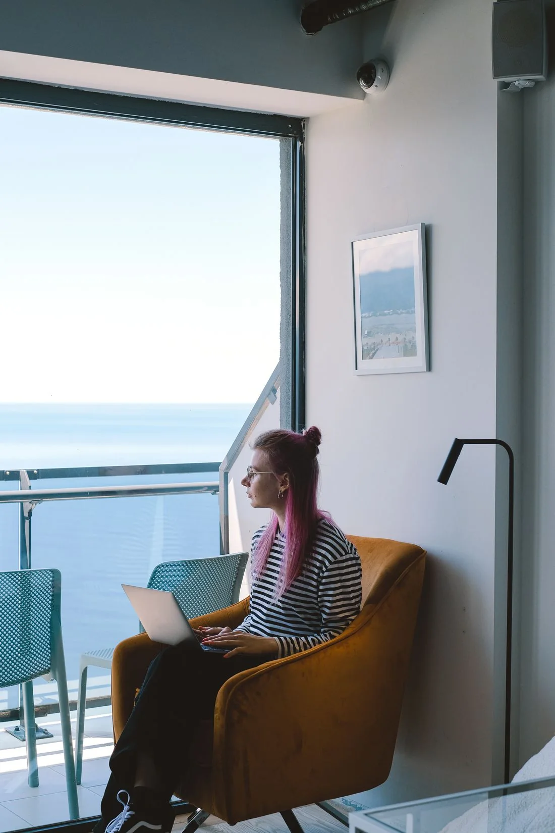 Woman working on a laptop beside a hotel window with an ocean view