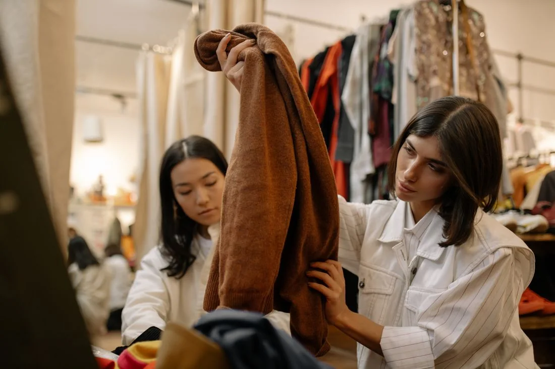 Two women examining vintage clothes in a thrift store