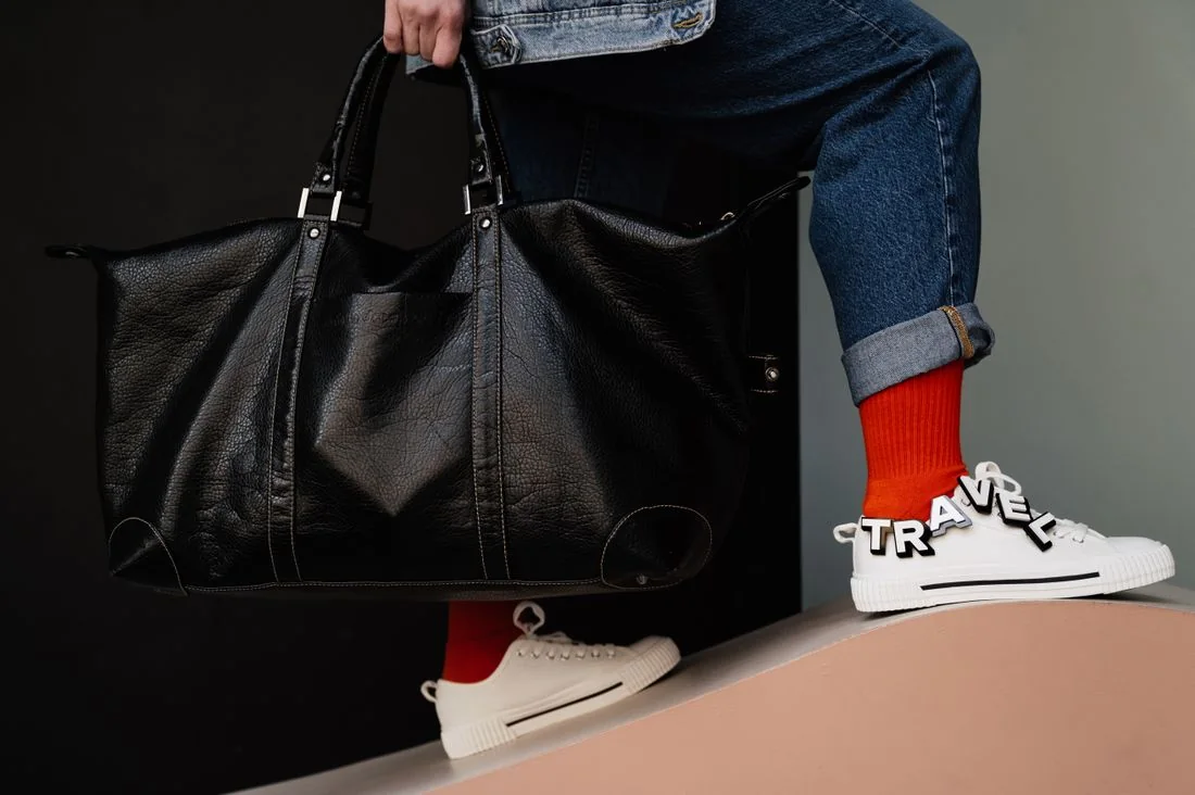 Traveler carrying a leather duffel bag beside casual sneakers